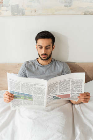 Young man in gray t-shirt reading newspaper on bedの写真素材