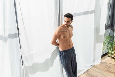 High angle view of shirtless and tattooed man looking at window