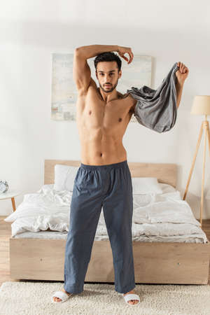 Bearded man taking off t-shirt in bedroomの写真素材