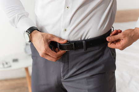Cropped view of businessman adjusting waist belt at homeの写真素材
