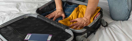 Cropped view of man pressing clothes in suitcase near passport and air ticket on bed, bannerの写真素材