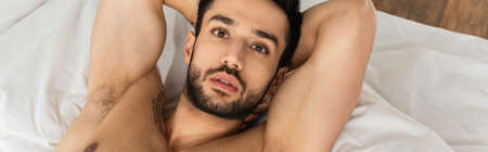 Top view of shirtless man lying on bed and looking at camera, bannerの写真素材