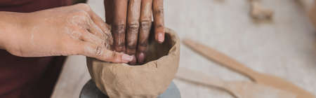 partial view of young african american woman sculpting clay pot with hands in pottery, bannerの写真素材