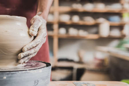 partial view of young african american man shaping wet clay pot on wheel in potteryの写真素材