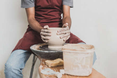 partial view of young african american man modeling wet clay pot on wheel in potteryの写真素材