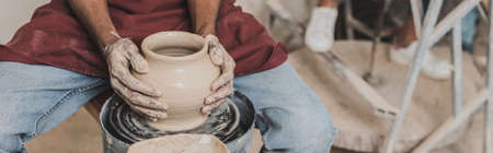 partial view of young african american man making wet clay pot on wheel in pottery, bannerの写真素材