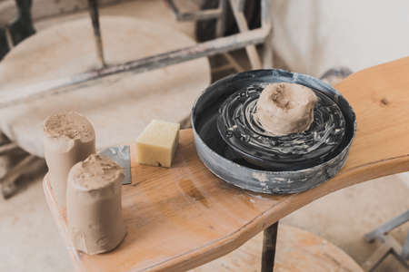high angle view of wet piece of clay on pottery wheel and sponge on wooden bench in art studioの写真素材