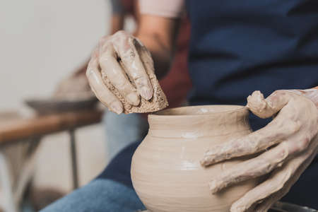 partial view of female african american hands shaping wet clay pot on wheel with sponge in potteryの写真素材