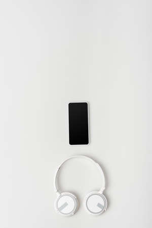 top view of wireless and modern headphones near smartphone with blank screen isolated on whiteの写真素材