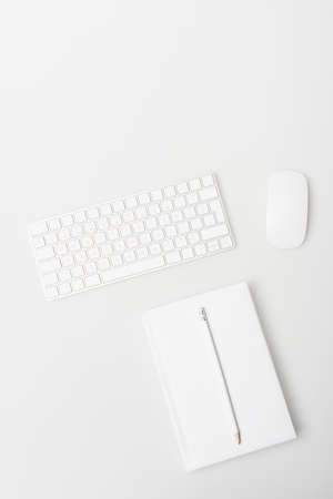 top view of computer mouse, keyboard and notebook with pencil isolated on white