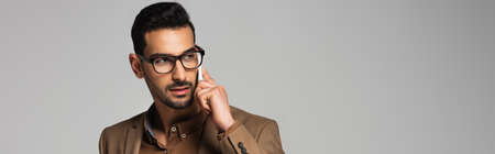 Muslim businessman talking on smartphone and looking away isolated on gray, banner