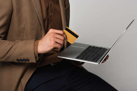 Cropped view of businessman with laptop and credit card isolated on grayの写真素材