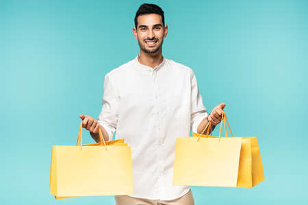 Positive arabian man holding yellow shopping bags isolated on blueの写真素材