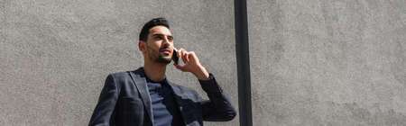 Young muslim businessman talking on mobile phone outdoors, bannerの写真素材