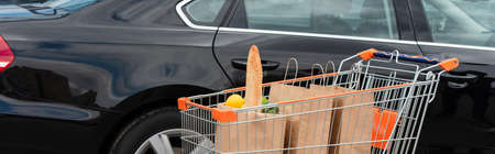 shopping trolley with fresh grocery near black car, bannerの写真素材