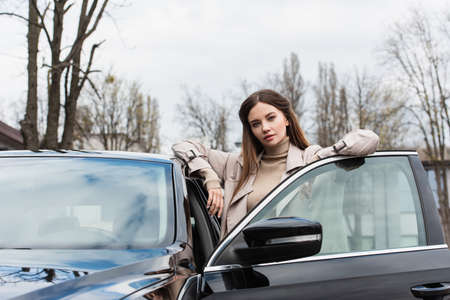 young woman looking at camera while standing near car outdoorsの写真素材