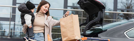 happy woman holding shopping bag and toddler son near car, bannerの写真素材