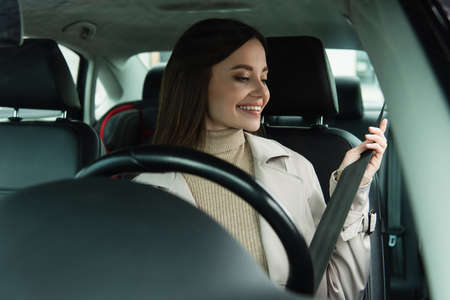 young woman adjusting seat belt while sitting in car