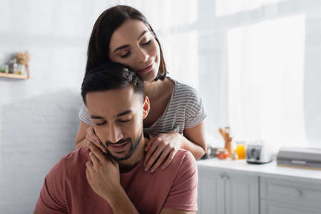 smiling young woman with closed eyes gently hugging boyfriend in kitchen