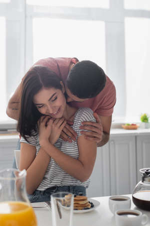 happy young couple hugging near table with breakfast, coffee and orange juice in kitchen