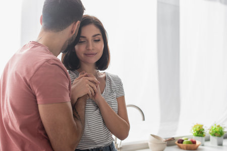 young brunette couple gently holding hands in kitchenの写真素材
