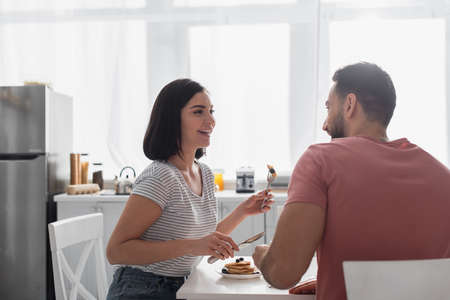 smiling young couple eating pancakes together in kitchenの写真素材