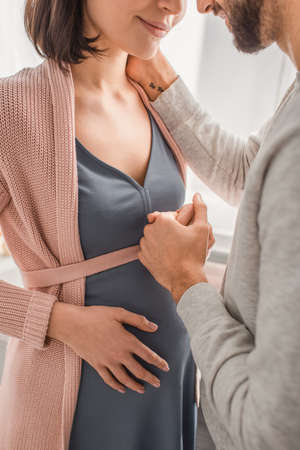partial view of young man gently holding hand of pregnant woman at home