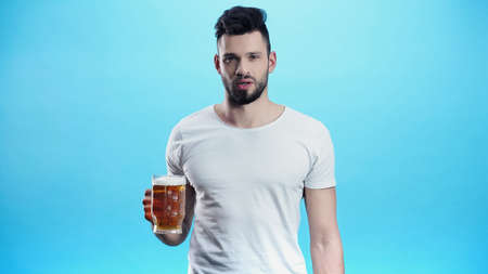 young man with mug of cold beer looking at camera isolated on blueの写真素材