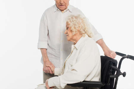 elderly woman in wheelchair holding hand of husband isolated on whiteの写真素材