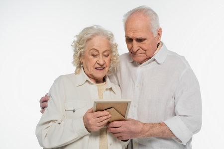 elderly couple holding photo frame in hands isolated on whiteの写真素材