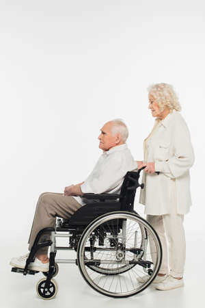 side view of elderly woman rolling husband in wheelchair on whiteの写真素材