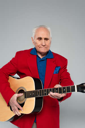 elderly man in red blazer holding acoustic guitar isolated on gray