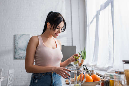 happy young woman holding sliced apple above blender jugの写真素材