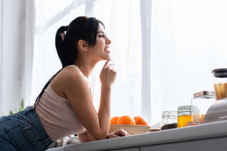 happy young and brunette woman looking away in kitchen
