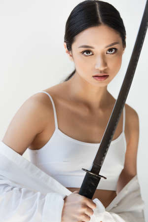 Young asian woman in white top and shirt holding sword isolated on grayの写真素材