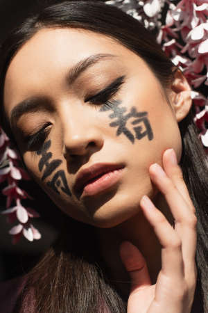 Portrait of asian woman with hieroglyphs on face and kanzashi isolated on blackの写真素材