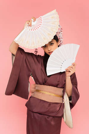 Young asian woman holding fans near face isolated on pinkの写真素材
