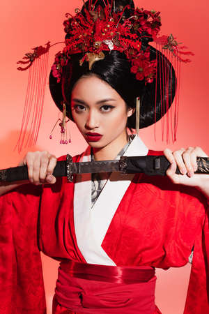 Asian woman in traditional kimono holding sword on red backgroundの写真素材