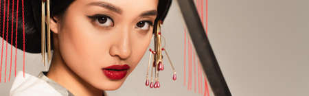 Japanese woman looking at camera near blurred sword isolated on gray, bannerの写真素材