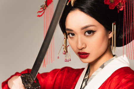 Asian woman with red lips holding sword on blurred foreground isolated on grayの写真素材