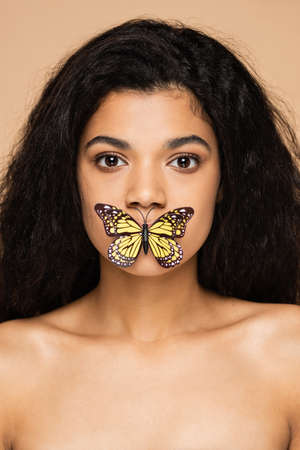 pretty african american young woman with butterfly on lips isolated on beige
