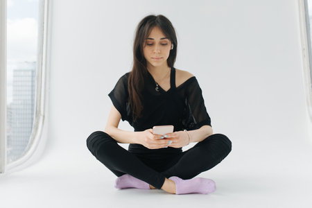 brunette armenian woman messaging on mobile phone while sitting with crossed legsの写真素材