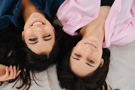 top view of two cheerful armenian women smiling at camera while lying togetherの写真素材