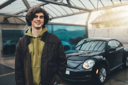Cheerful man looking at camera near blurred car on self service wash