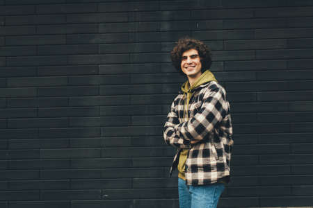Cheerful man standing with crossed arms near black brick wall