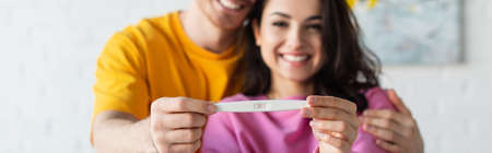 pregnancy test in hands of blurred smiling young couple at home, bannerの写真素材