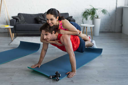 smiling fit young woman lying on back of man doing plank at homeの写真素材