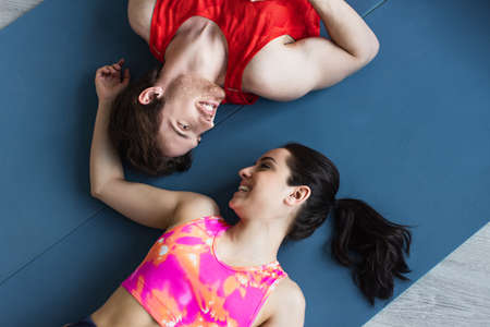 top view of young couple in sportswear lying on fitness mats and looking at each other at home