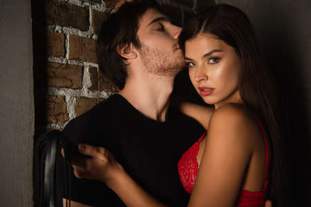 seductive woman with flogging whip looking at camera near young man in darkness