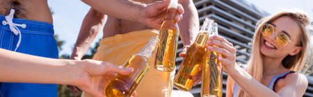 Blurred friends in swimming trunks toasting with beer bottles outdoors, bannerの写真素材